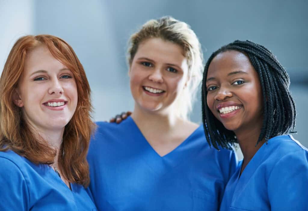 Three women wearing blue medical scrubs stand together smiling, representing the dedicated P4F Homecare Champions care team of healthcare professionals.